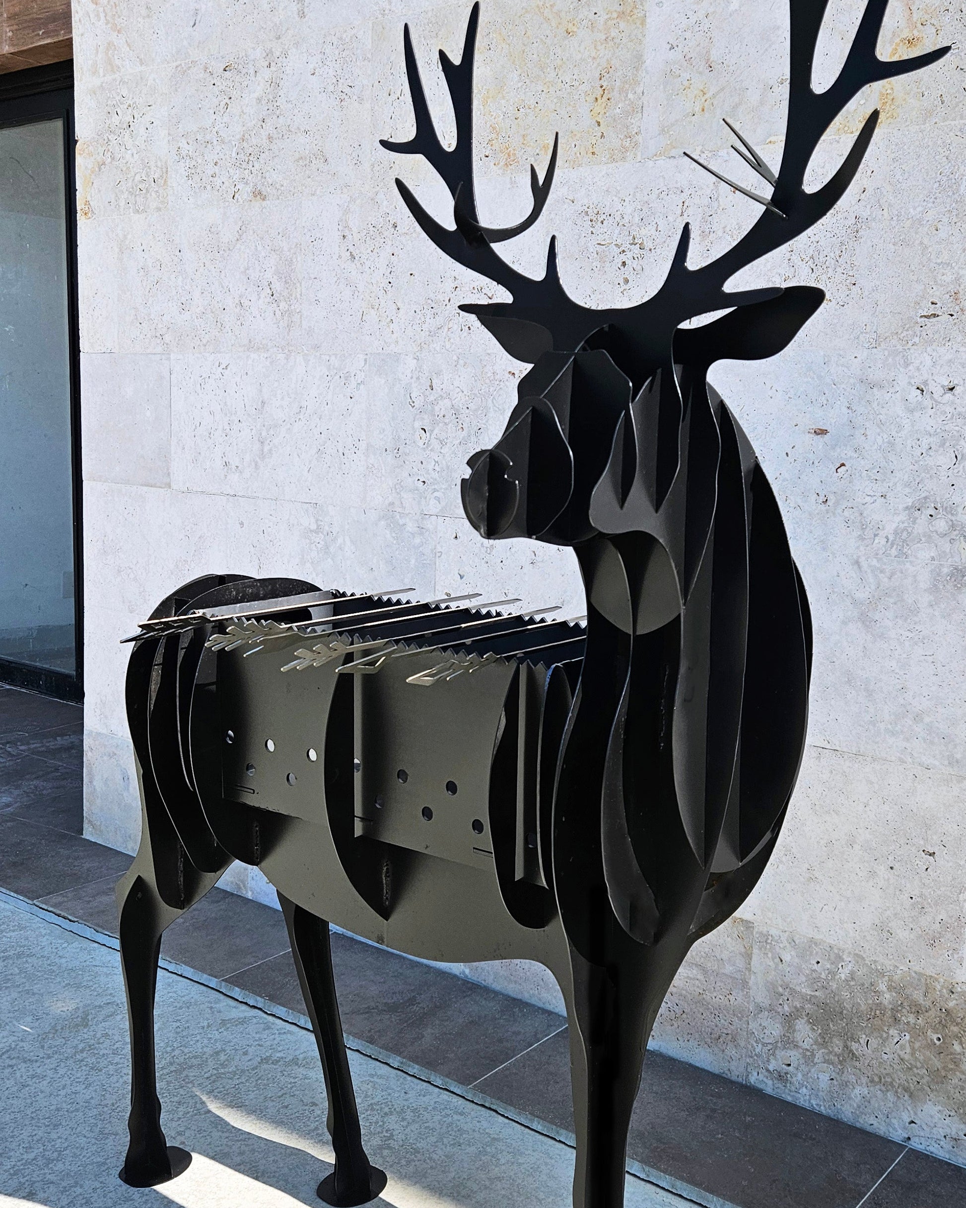 Black deer-shaped grill against a light stone wall.